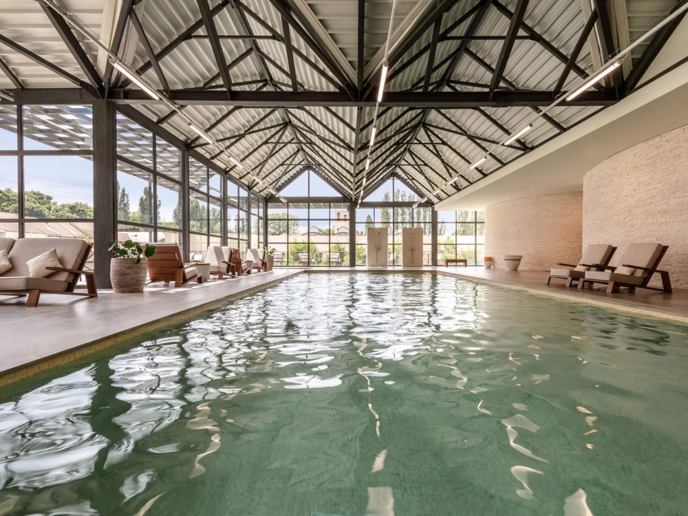 La piscine intérieure du spa du Grand Pavillon Chantilly, sous sa charpente métallique et ses baies vitrées