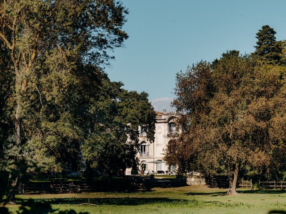 La façade du Domaine de Biar entre de grands arbres, sur une pelouse de son parc