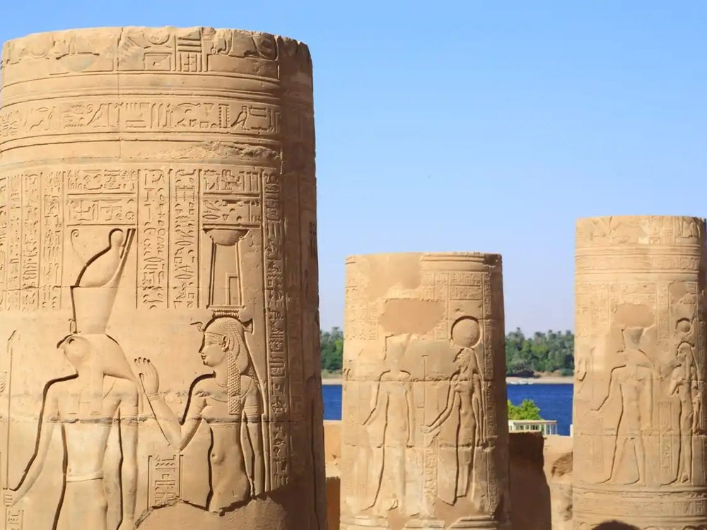Les colonnes gravées du temple de Kom Ombo, hiéroglyphes et bas-reliefs, le Nil et la rive verte derrière