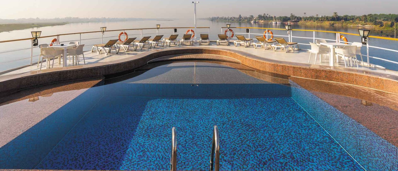 La piscine et les transats du pont soleil du RV Star of Luxor à l'aube, le Nil et la rive plate en arrière-plan