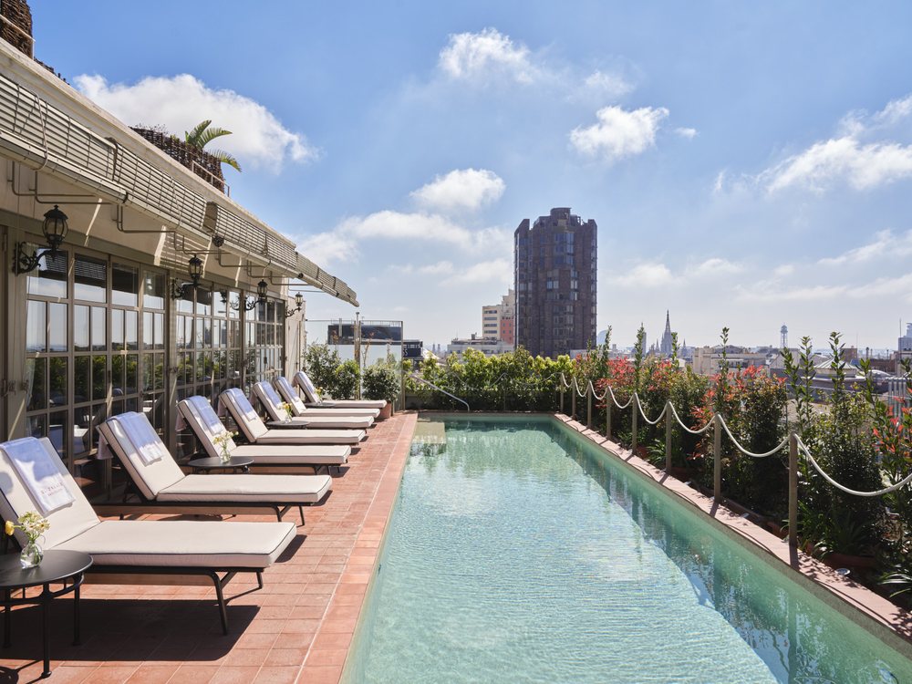 La piscine sur le toit d'El Palace Barcelona, ses transats et ses voiles, avec la ville en contrebas