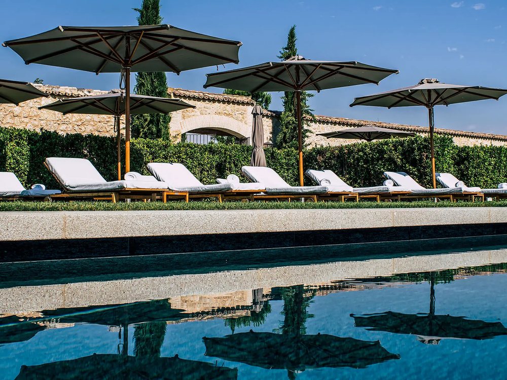 La piscine extérieure d'Abadía Retuerta, ses parasols et ses transats devant les murs de l'abbaye