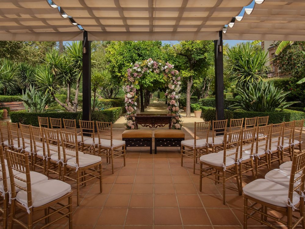 Une cérémonie préparée sous une pergola dans les jardins de l'Hotel Alfonso XIII, arche fleurie et chaises