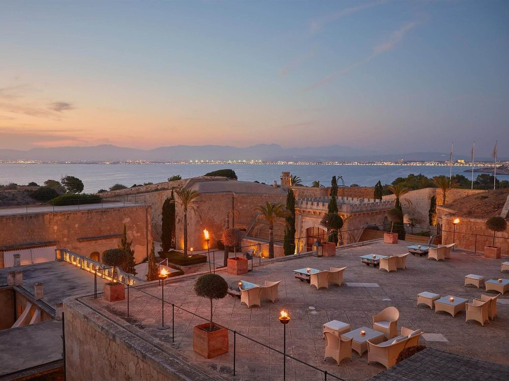 La terrasse de la forteresse de Cap Rocat au crépuscule, torches allumées, la baie de Palma au fond