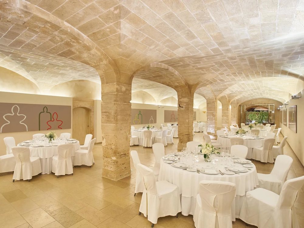 Une salle voûtée du Zoëtry Mallorca dressée pour un banquet, tables rondes nappées de blanc
