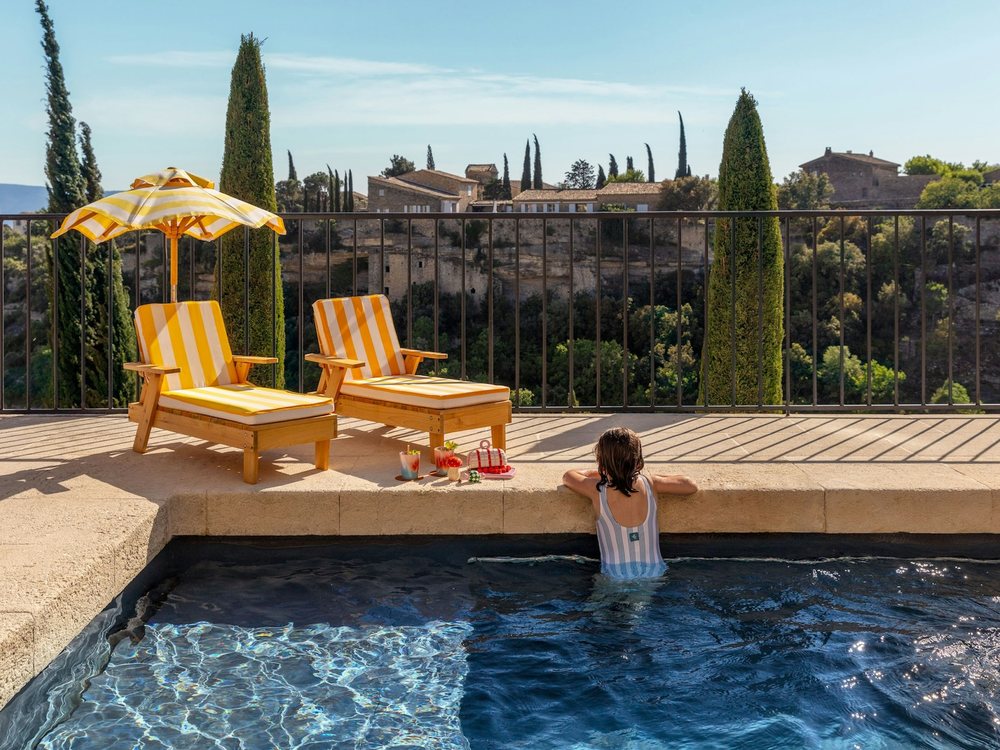 Une fillette dans la piscine du Summer Camp de La Bastide, à Gordes, devant les transats jaunes et les cyprès