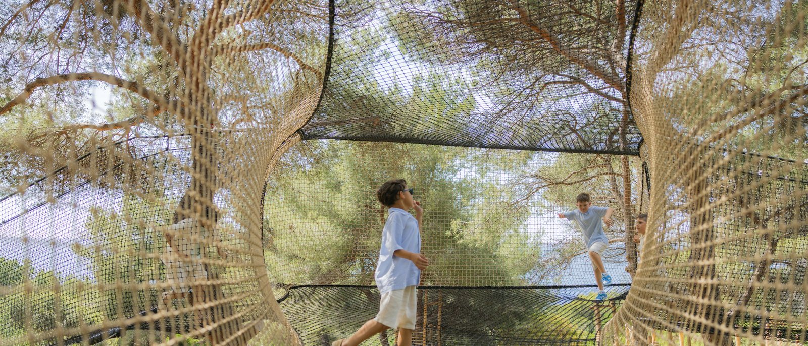 Deux enfants sur les filets suspendus du Kids Club du Grand-Hôtel du Cap-Ferrat, entre les pins, au-dessus de la Méditerranée