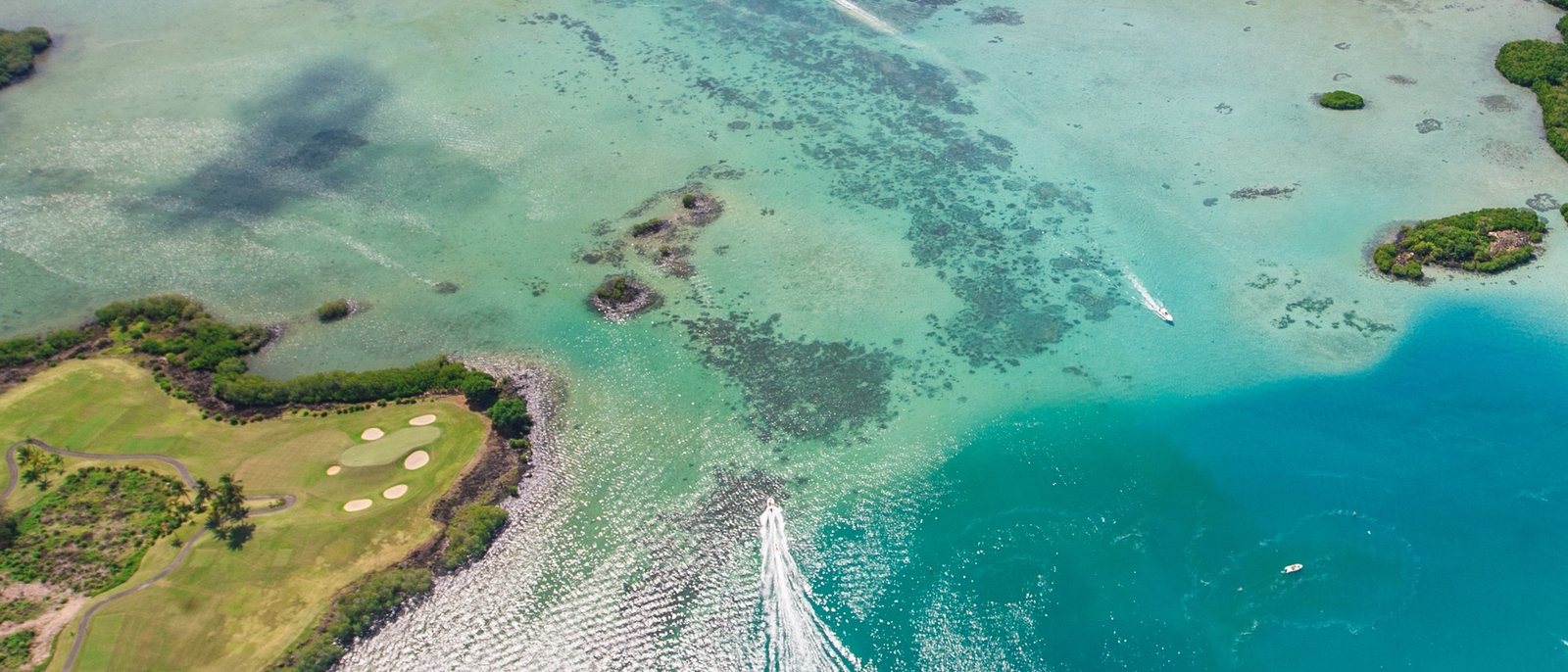 Un trou de l'Ile aux Cerfs Golf Club au bord du lagon, vu du ciel, avec les récifs et un bateau dans l'eau turquoise