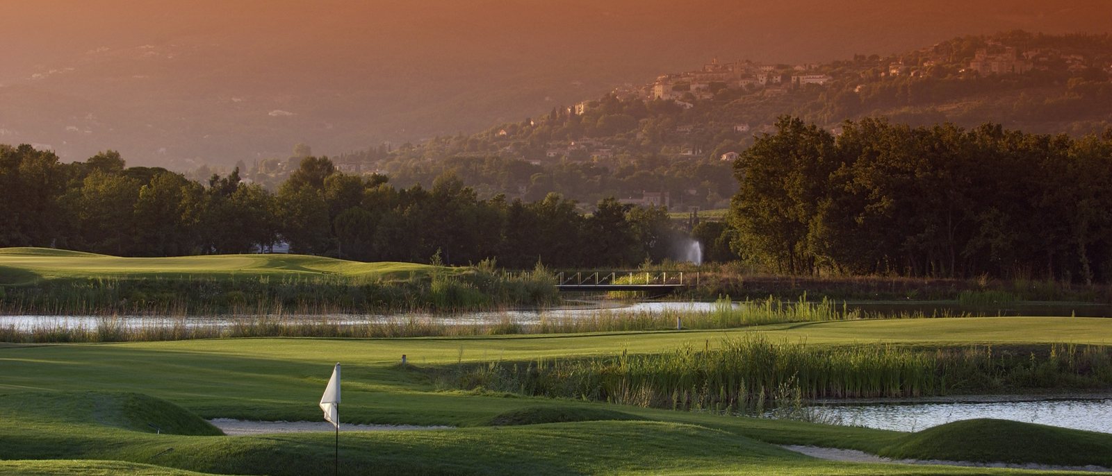 Le parcours du Château de Terre Blanche au coucher du soleil, ses plans d'eau et ses pins, face aux collines du Pays de Fayence
