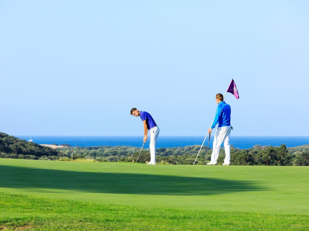 Deux golfeurs sur un green du Murtoli Golf Links, le drapeau violet devant la mer et le maquis