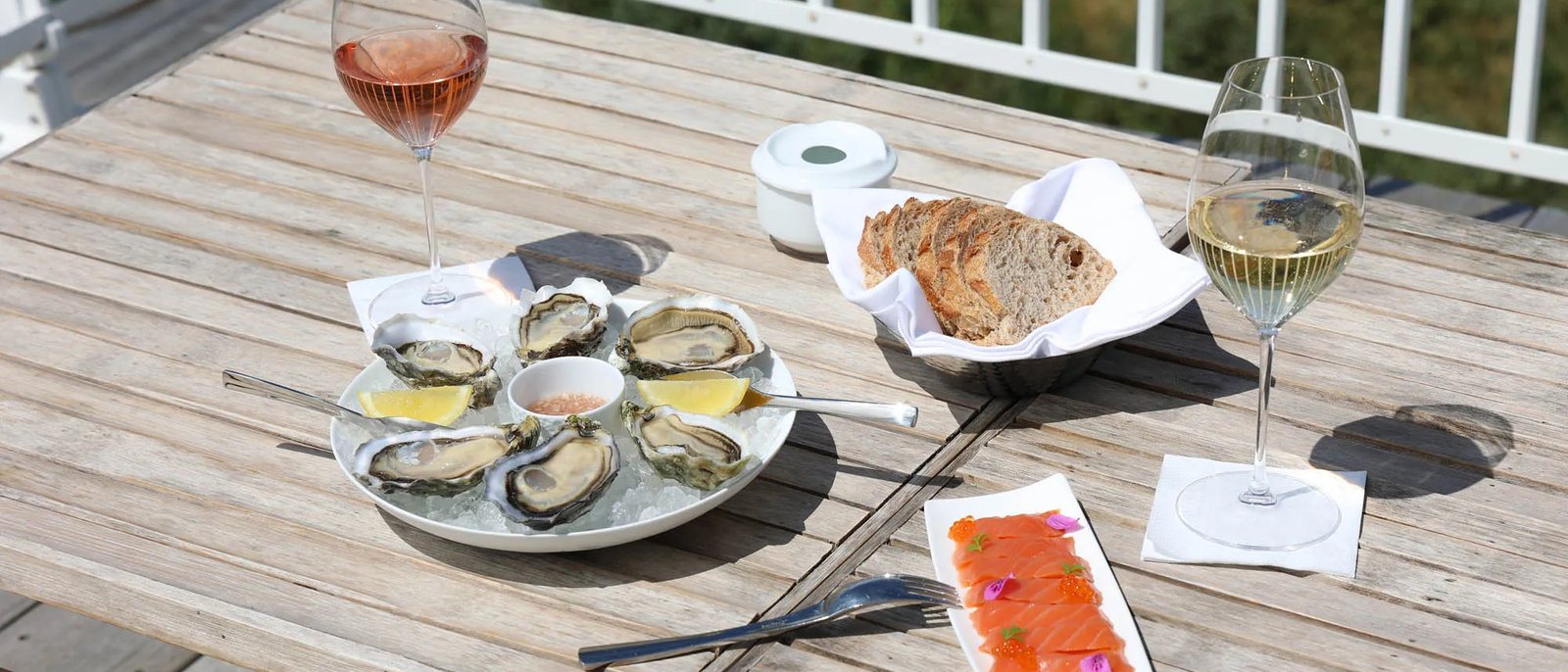 Des huîtres sur un lit de glace, du pain et deux verres de vin sur une table en bois de la terrasse du Grand Large