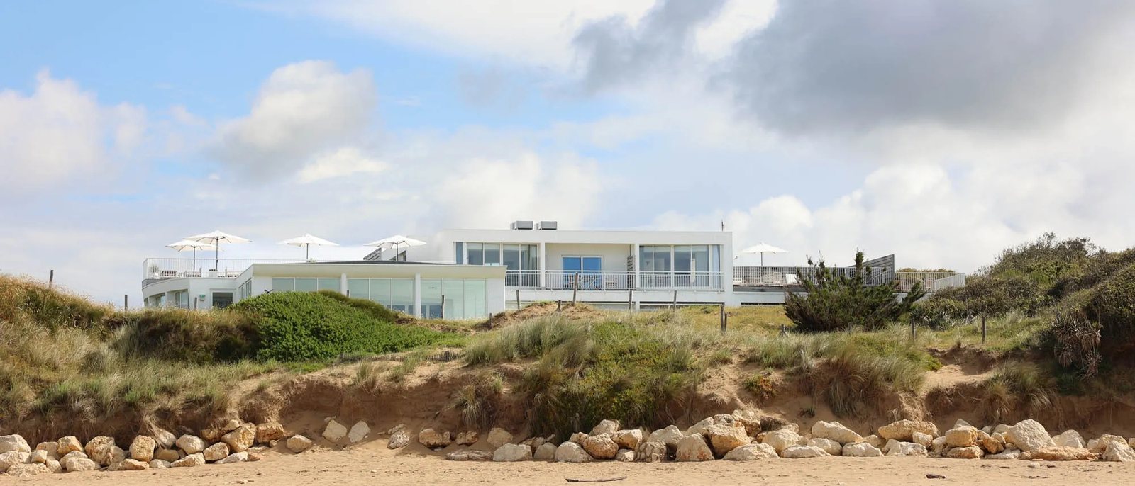 Le Grand Large vu depuis la plage de la Rémigeasse, ses façades blanches au sommet de la dune et ses parasols sur les terrasses
