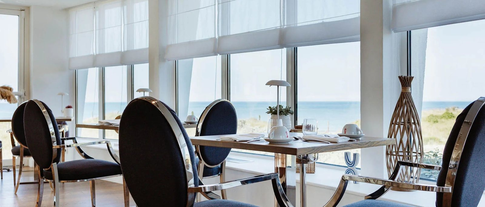 La salle de La Table du Grand Large, ses fauteuils médaillon noirs, ses tables dressées et les baies ouvertes sur la plage et l'océan