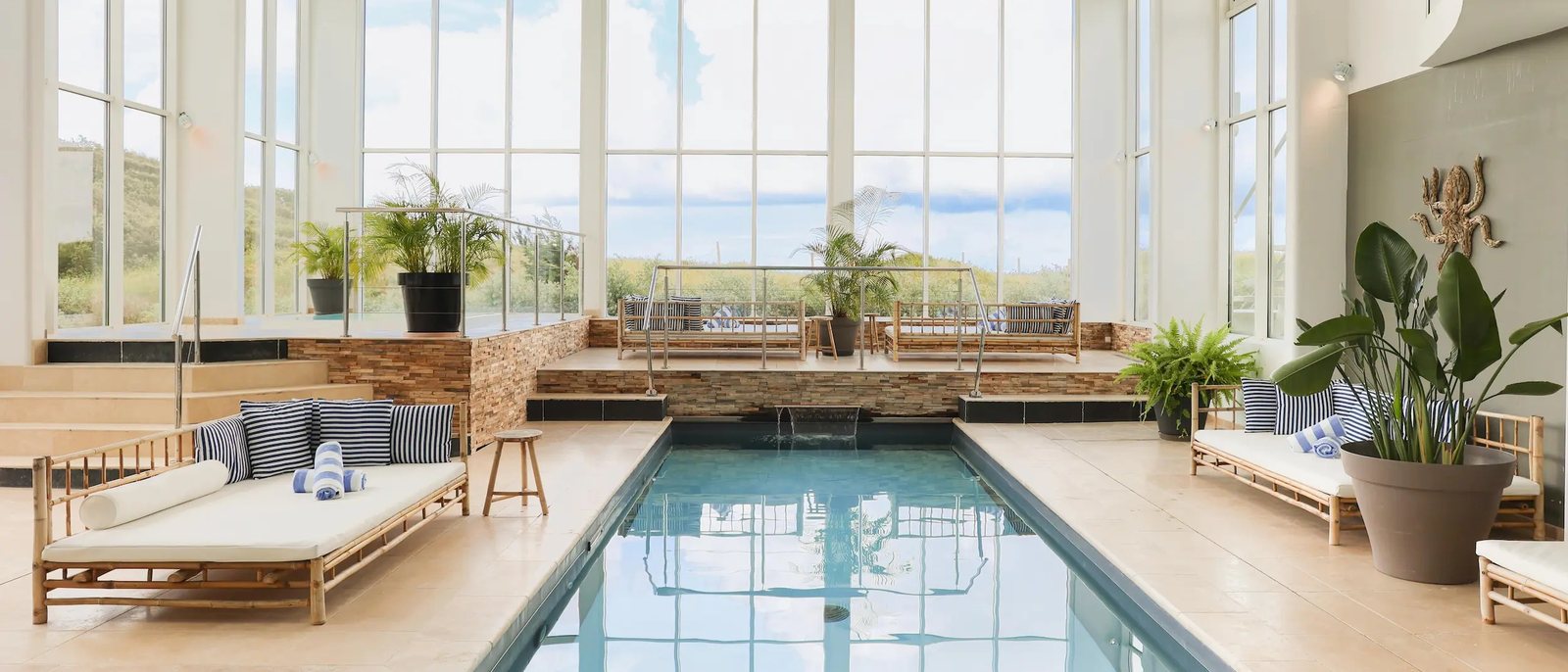 La piscine chauffée du Grand Large sous sa verrière, ses lits de repos en bambou, ses plantes et les dunes derrière les baies
