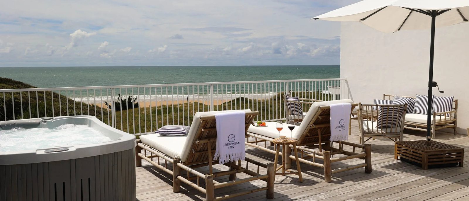 Une terrasse du Grand Large avec son bain bouillonnant, ses bains de soleil et son parasol, face aux dunes et à l'océan
