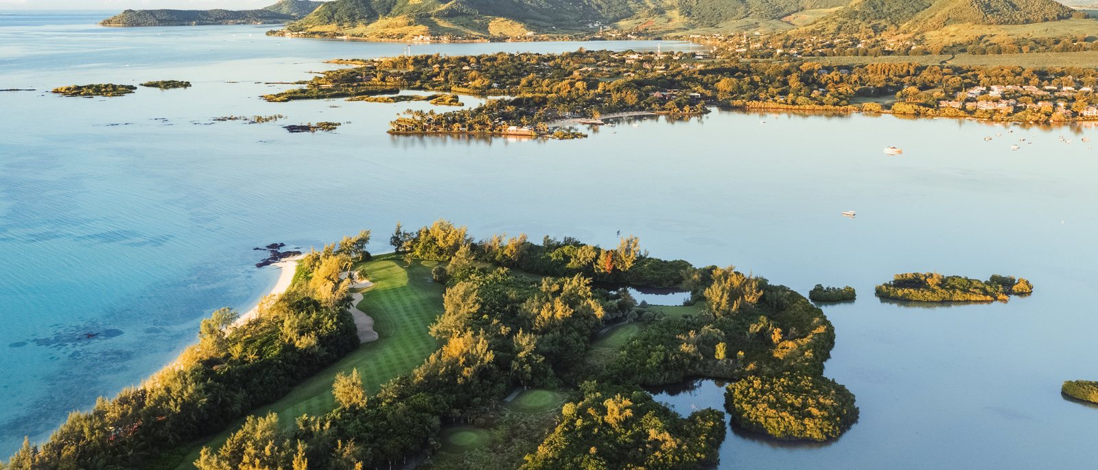 L'île aux Cerfs vue du ciel au lever du jour, le parcours de golf dans la végétation, le lagon et les montagnes de la côte est de l'île Maurice