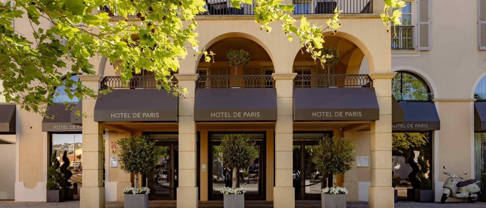 La façade à arcades de l'Hôtel de Paris Saint-Tropez, ses stores au nom de l'hôtel et ses oliviers en pot