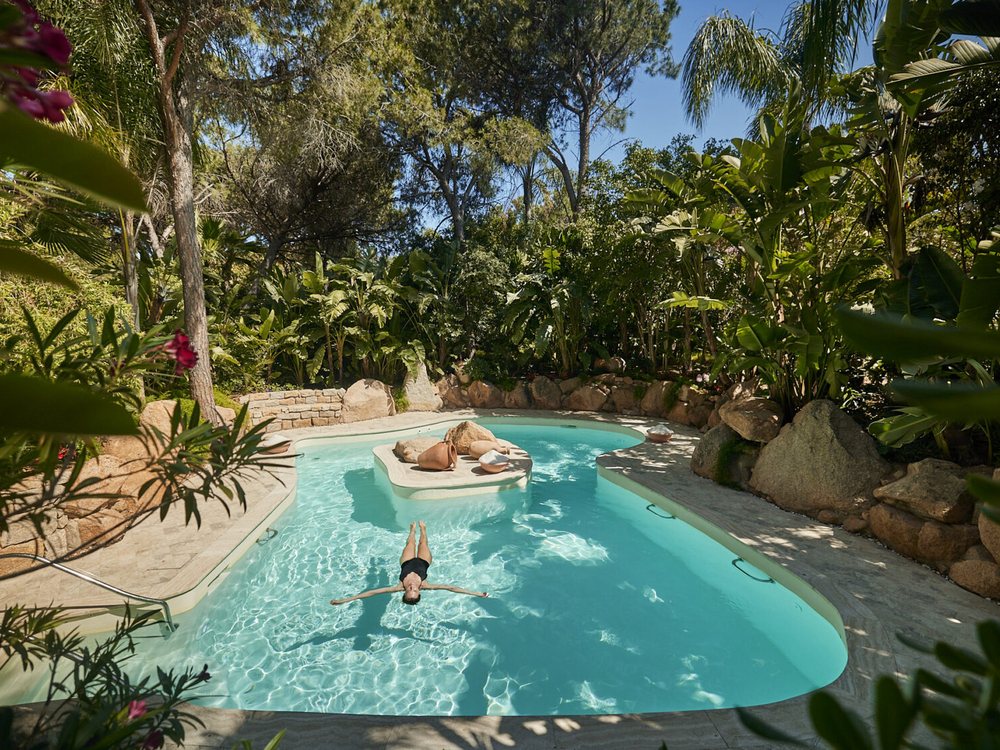 Une baigneuse dans un bassin d'eau de mer du spa Acquaforte de Forte Village, entre rochers et végétation