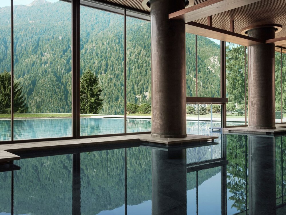 La piscine intérieure du Lefay Resort & SPA Dolomiti, ses colonnes et sa baie vitrée ouverte sur la forêt