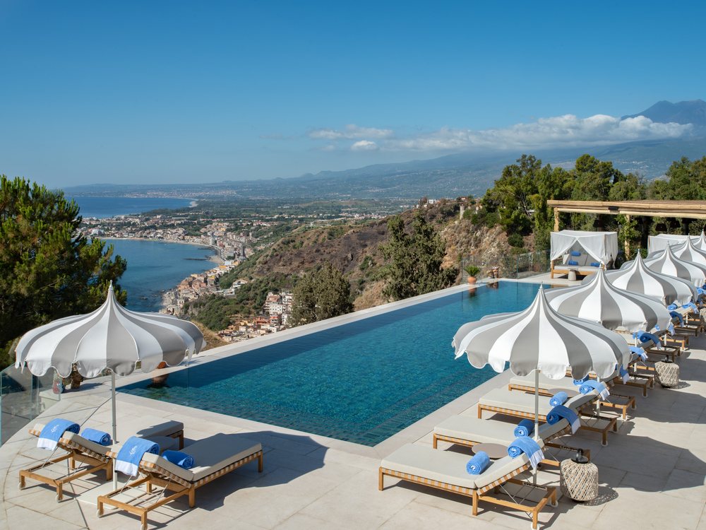 La piscine à débordement du San Domenico Palace et ses parasols blancs, au-dessus de la baie de Taormine et de l'Etna