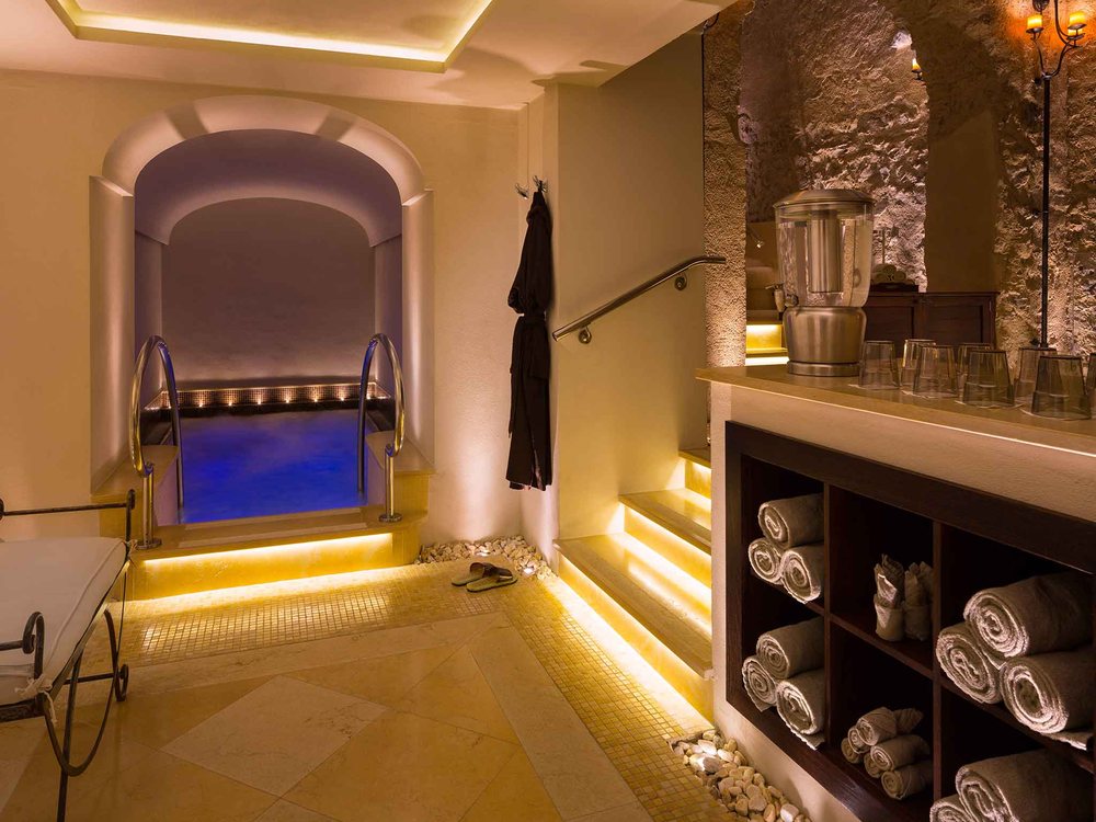 Le bassin d'hydrothérapie voûté du spa du Monastero Santa Rosa, éclairé de bleu, sous une arche de pierre