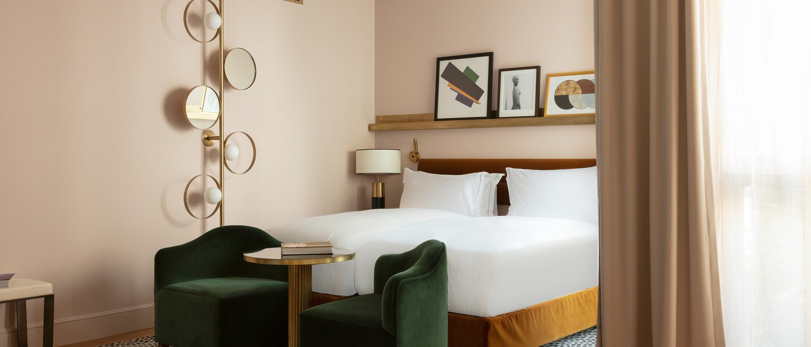 Une chambre Contemporaine des Jardins du Faubourg, aux murs rose poudré, avec ses fauteuils verts et son luminaire de laiton