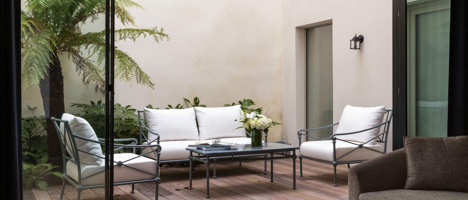 La terrasse privée de la suite La Villa Faubourg, en rez-de-jardin, avec ses fauteuils blancs et ses fougères