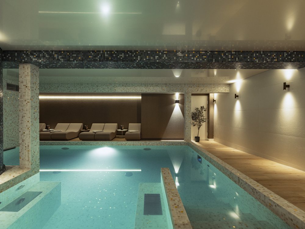 La piscine intérieure du spa d'Amoria à La Baule, éclairée de bleu, bordée de transats blancs sous un plafond lumineux
