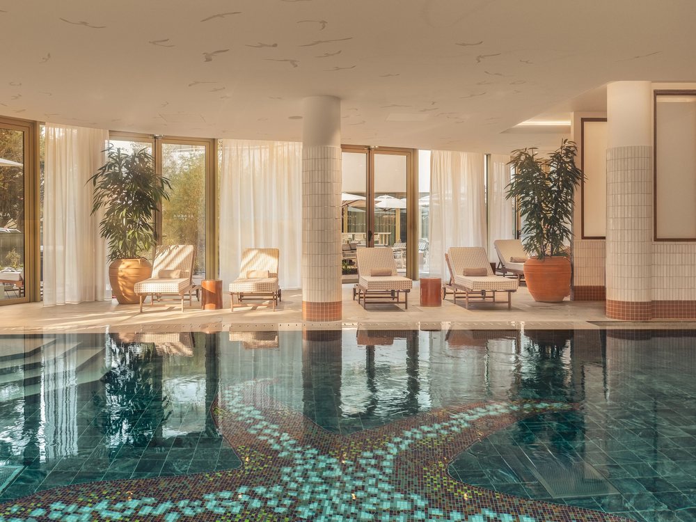 La piscine intérieure du spa Alaena des Cimes Bleues, sa mosaïque au fond du bassin, ses colonnes et ses palmiers en pot