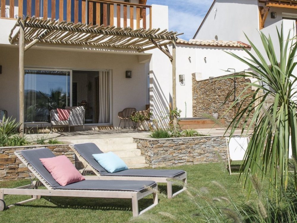 La terrasse d'une suite côté jardin, ses transats et ses coussins colorés sous une pergola