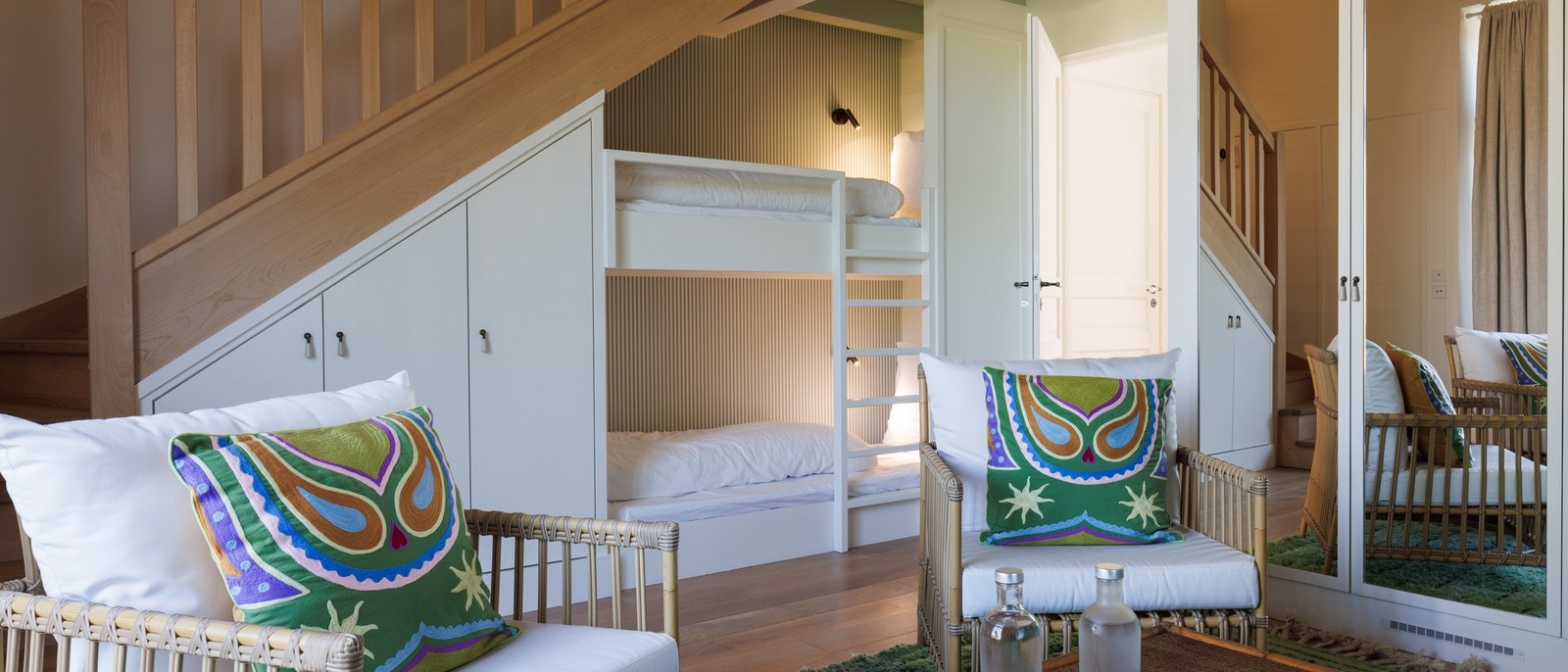 Une suite en duplex de La Mission, escalier de bois clair, lits superposés et fauteuils de rotin aux coussins brodés