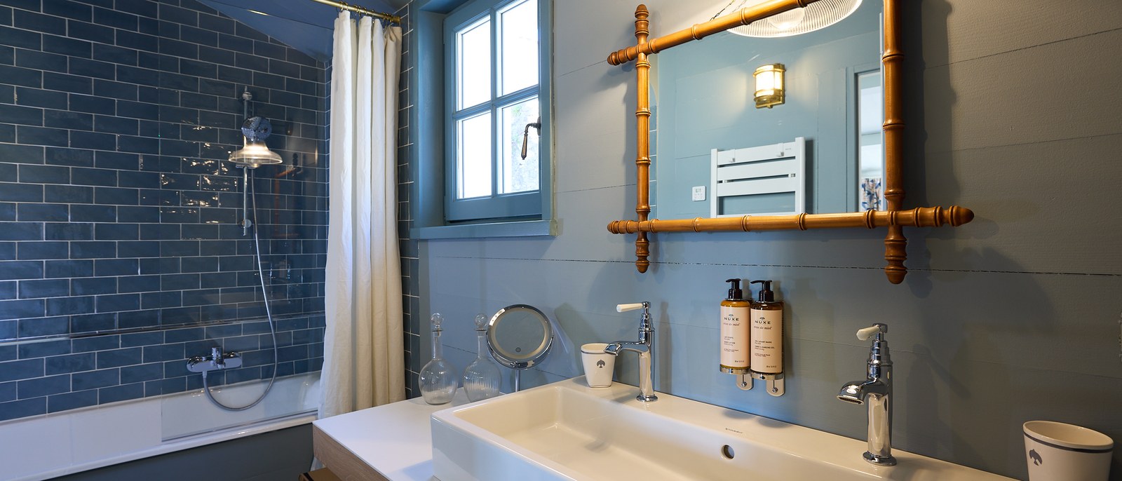 Une salle de bain de La Mission, carreaux bleus, double vasque et miroir encadré de bambou