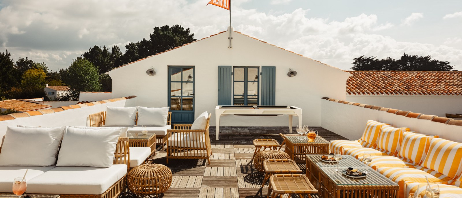La Vigie, rooftop de La Mission, banquettes à coussins rayés jaunes et tables basses sur un plancher de bois