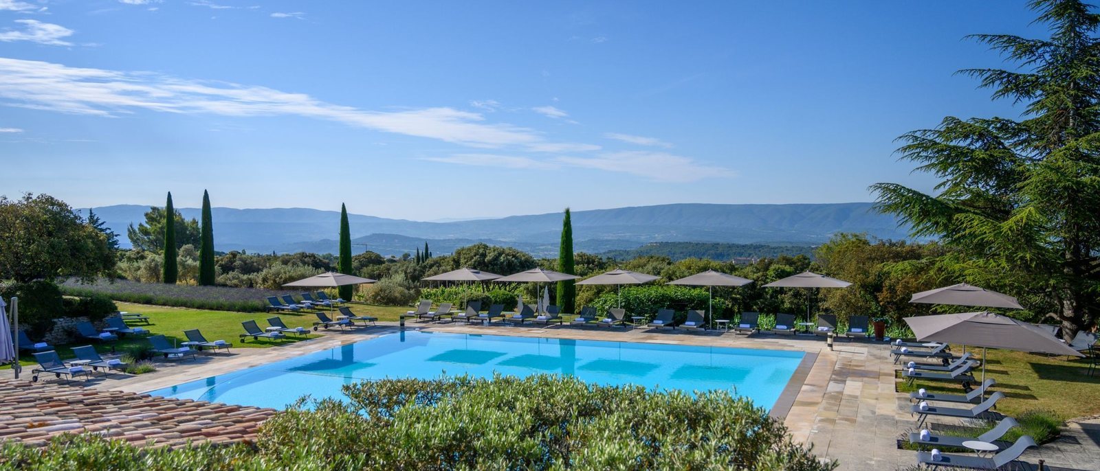 La piscine extérieure des Bories, à Gordes, ses transats et ses cyprès face à la vallée du Luberon
