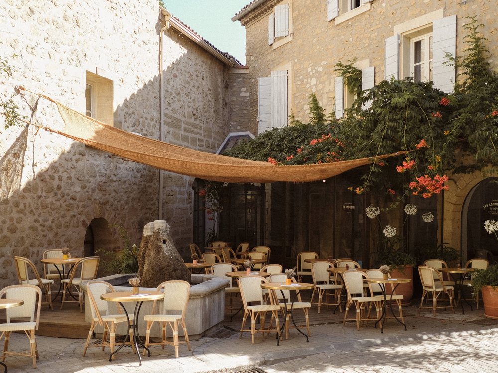 La terrasse ombragée du Moulin, à Lourmarin, ses tables de bistrot sous un voile de toile, entre les façades de pierre