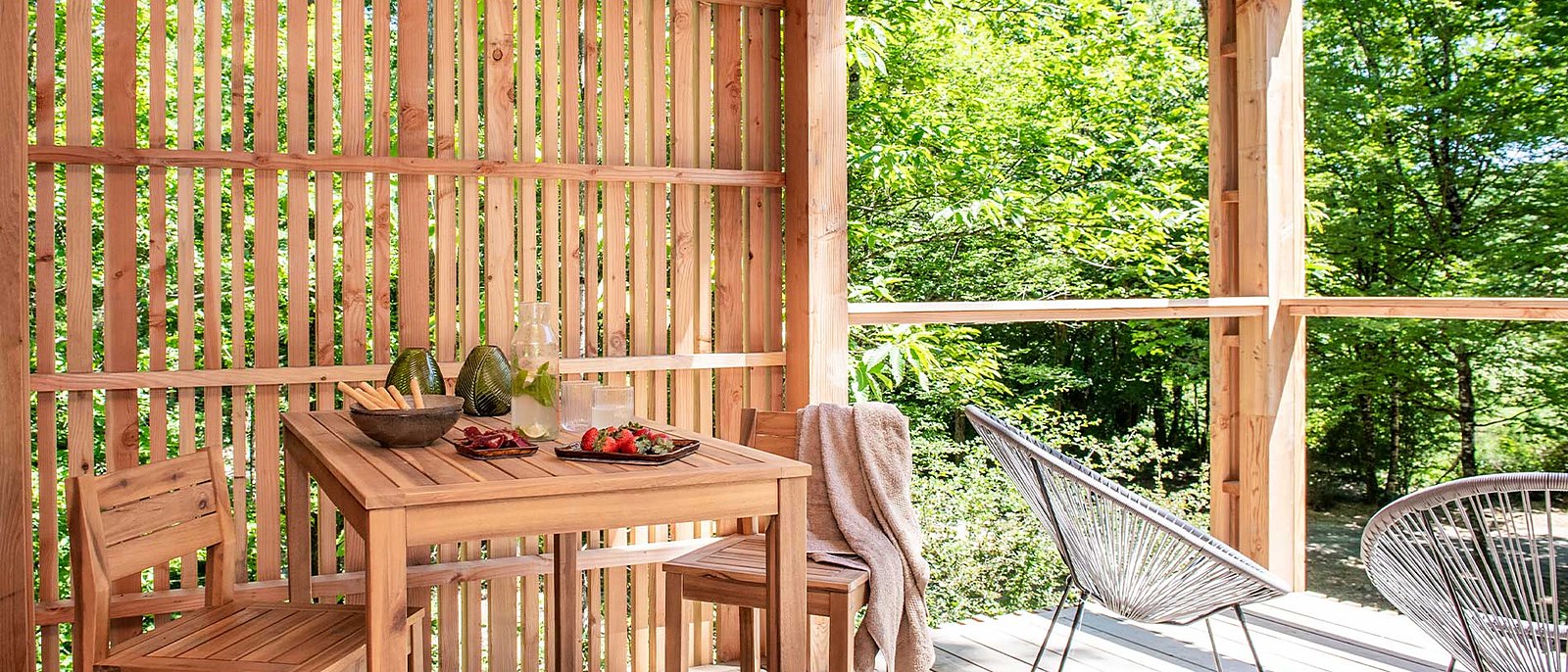 Une terrasse de lodge dressée pour un repas, sous sa claustra de bois, face à la forêt