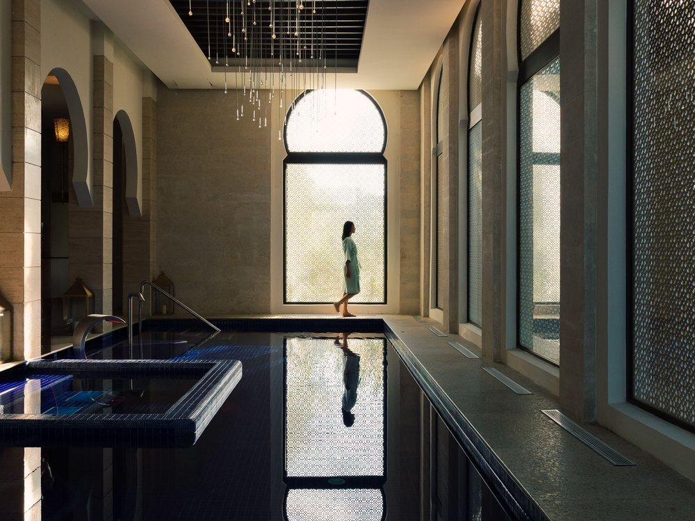 Le bassin intérieur du spa du Banyan Tree Tamouda Bay, ses hautes fenêtres et une silhouette devant la lumière