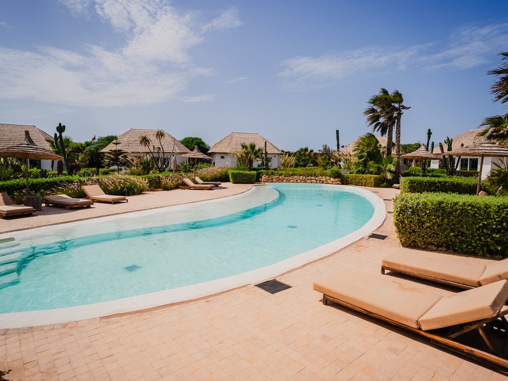 La piscine de La Crique à Dakhla, sa forme libre, ses transats et ses pavillons aux toits de chaume
