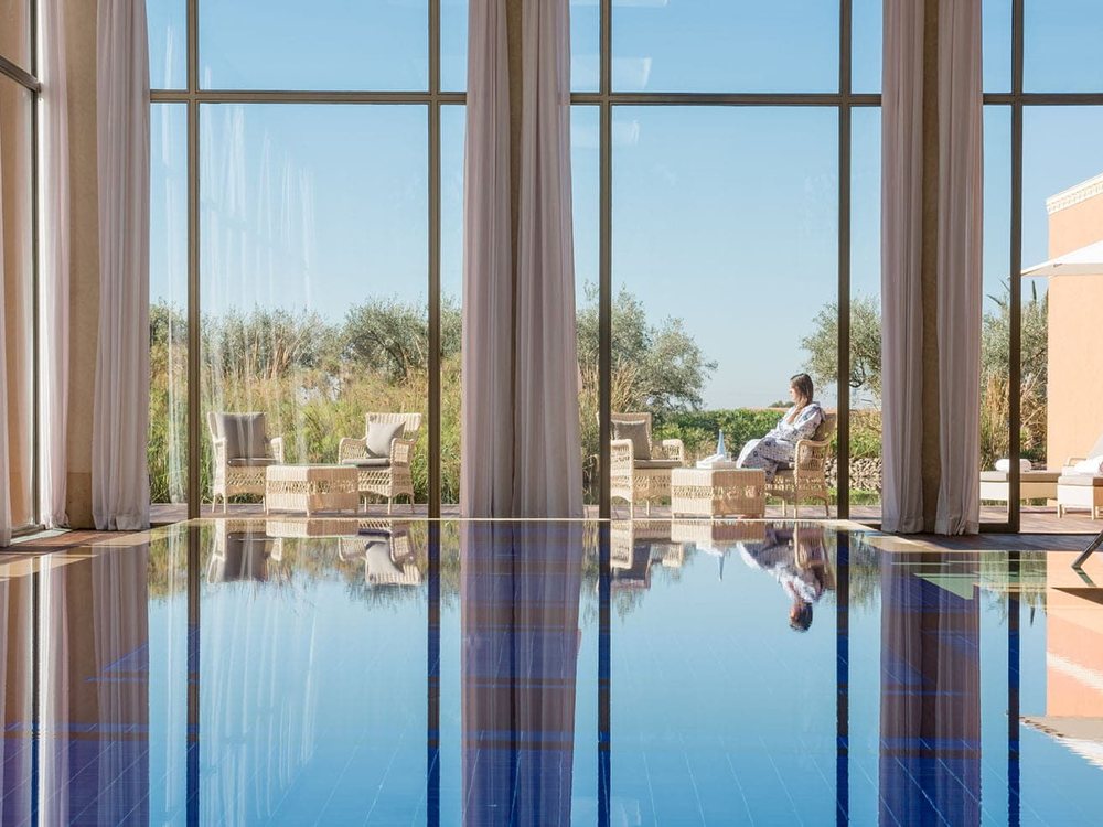 La piscine intérieure du spa de The Oberoi Marrakech, ses grandes baies et ses rideaux ouverts sur le jardin