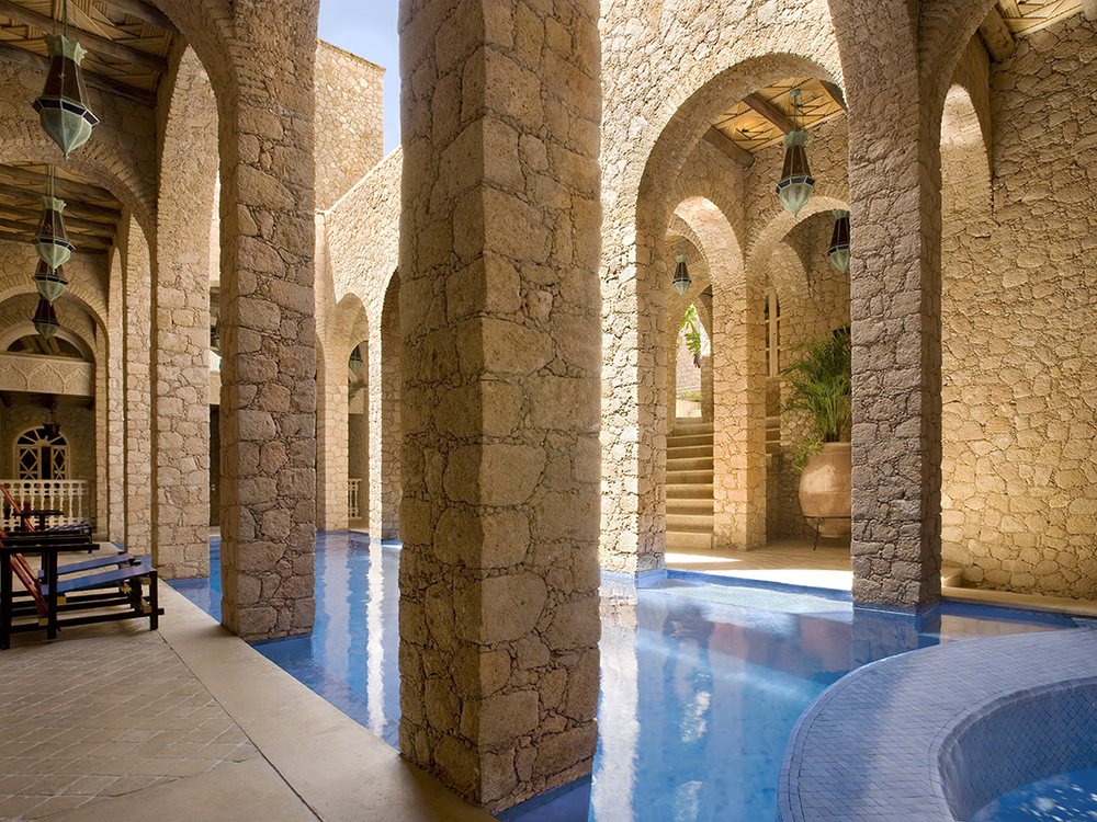 La piscine intérieure du spa de La Sultana Oualidia, entre de hauts piliers de pierre et des arches