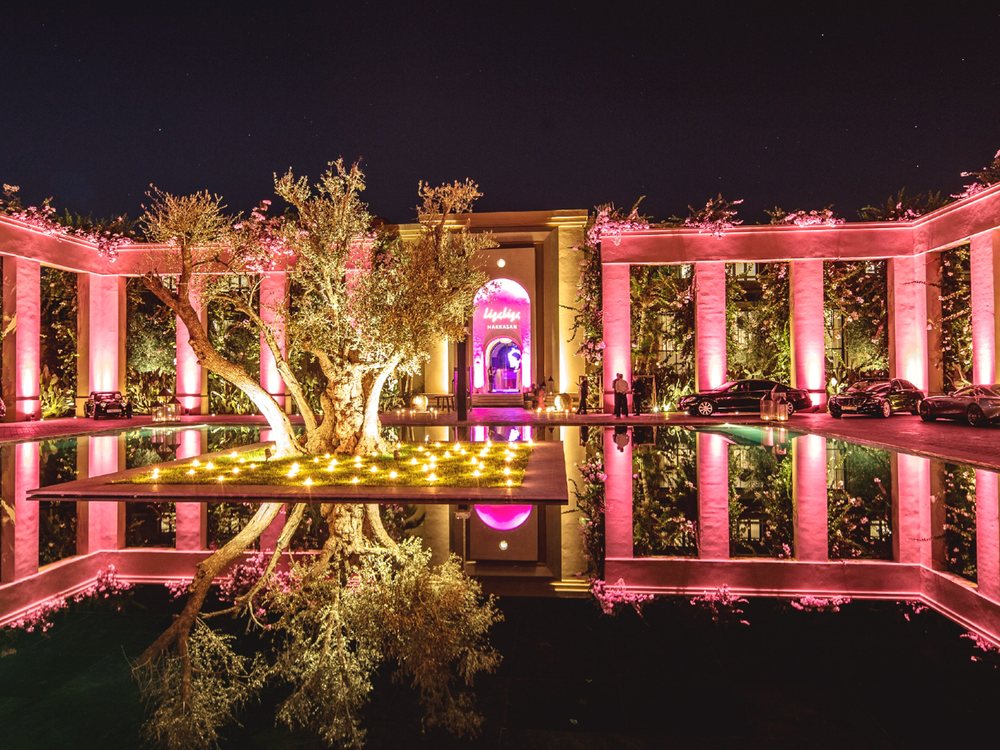 La Cour Carrée du Mandarin Oriental, Marrakech, de nuit : colonnade éclairée de rose, bassin et olivier