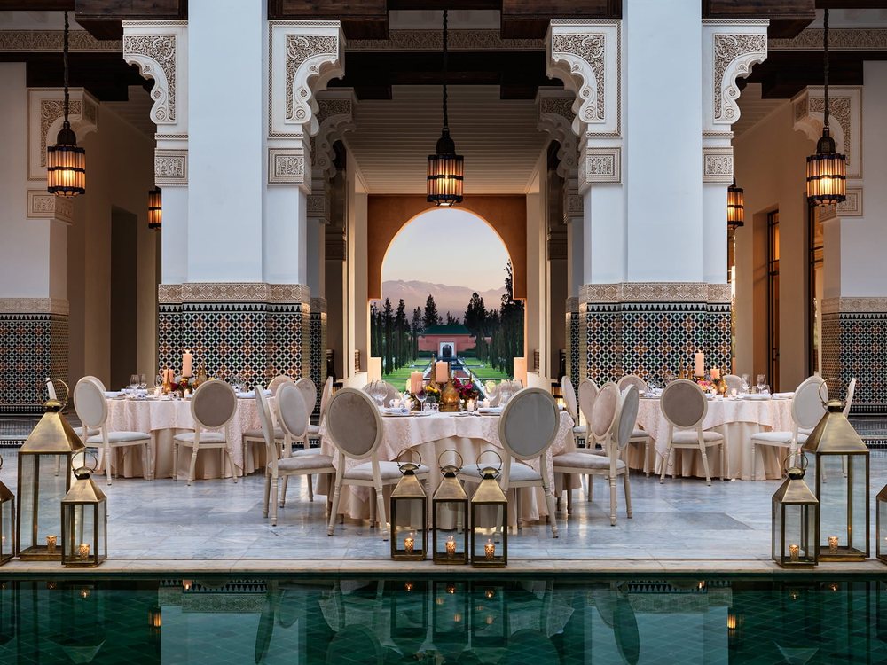Le patio de The Oberoi, Marrakech, dressé pour un dîner de réception entre les arcades, l'Atlas dans l'encadrement