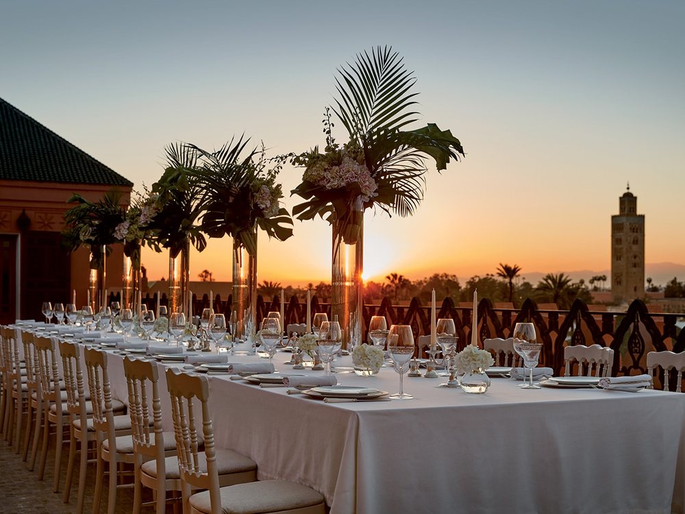 Une longue table de mariage dressée sur un toit-terrasse du Royal Mansour au coucher du soleil, la Koutoubia au loin