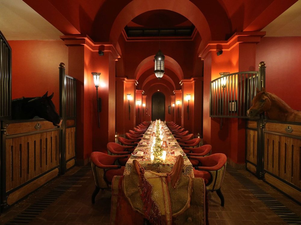 Une longue table dressée aux chandelles dans l'allée des écuries du Selman Marrakech, des pur-sang dans leurs boxes