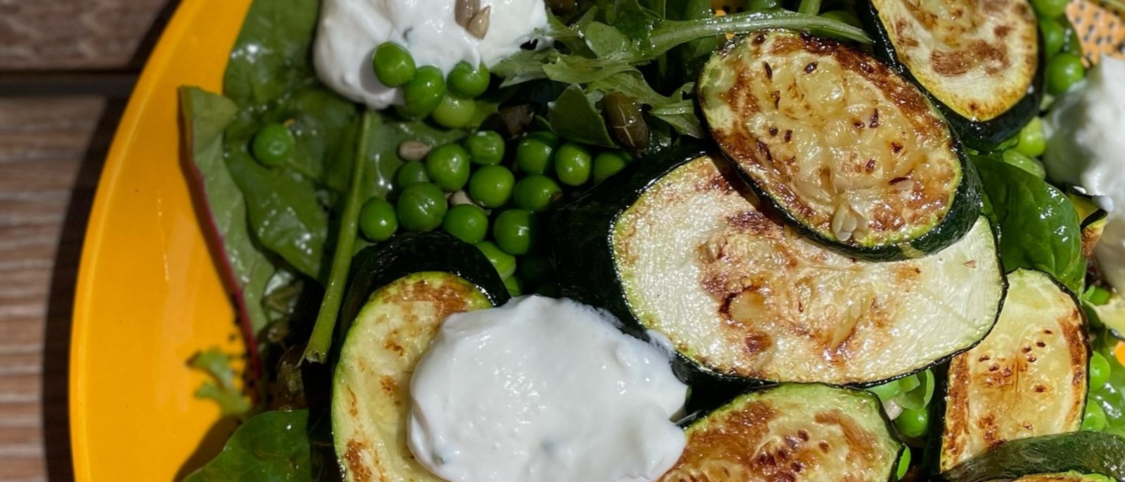Une assiette de courgettes grillées, petits pois, roquette et fromage frais sur une assiette jaune