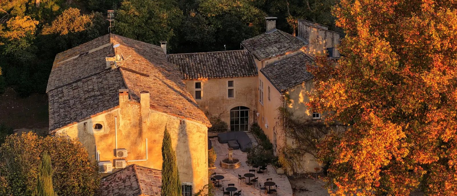 Le Mas des Prêcheurs vu du ciel à l'automne, ses toits de tuiles, sa cour et les arbres roux autour