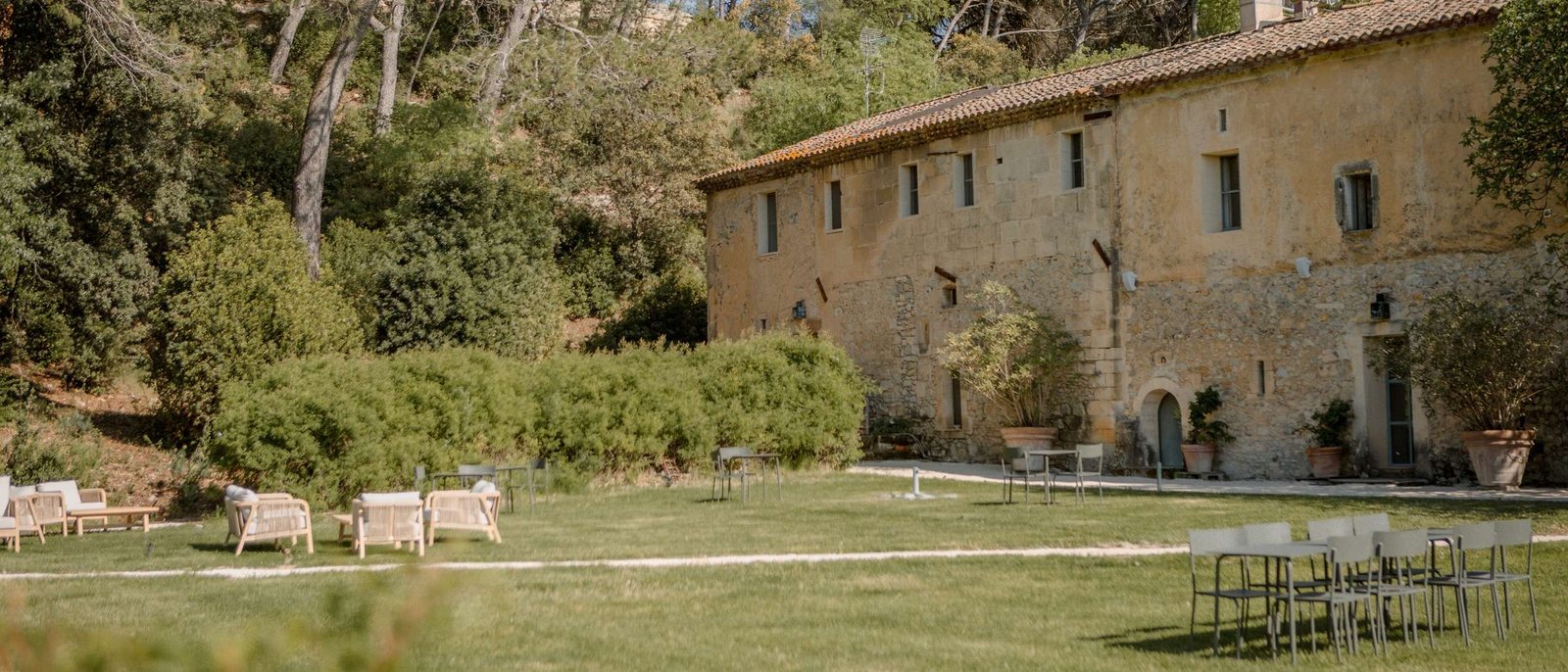 La façade de pierre du Mas des Prêcheurs, sa pelouse, ses transats et sa grande table sous les arbres