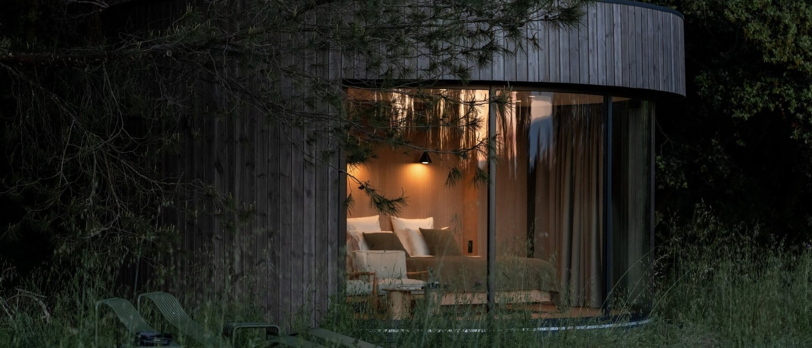 Une suite immersive du Mas des Prêcheurs à la tombée du jour, cocon de bois arrondi aux grandes baies éclairées dans les herbes