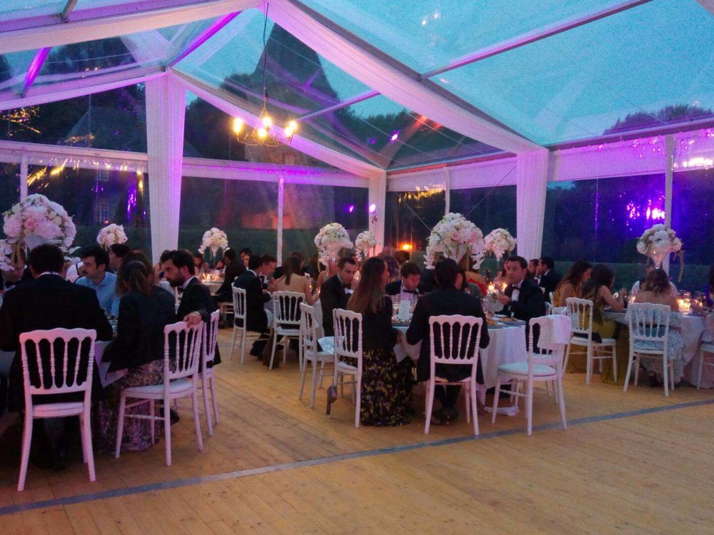 Un dîner de mariage sous une tente transparente éclairée de violet, dans le parc du Château de Canisy