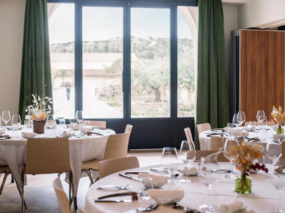 La salle de réception du Château l'Hospitalet dressée en tables rondes, ses portes vitrées ouvertes sur les oliviers